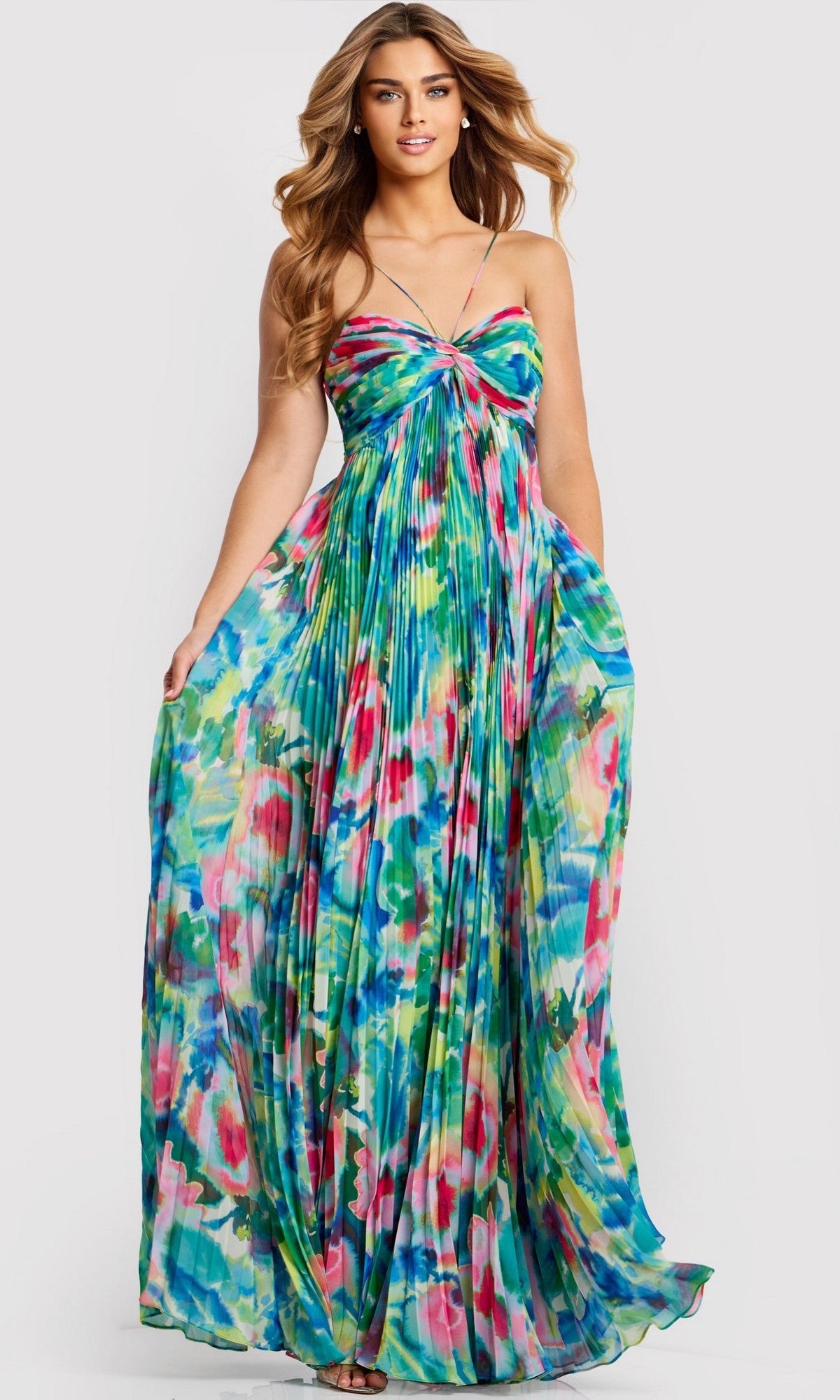 A woman wearing the Jovani 42558 long prom dress, featuring pleated chiffon, thin straps, and a vibrant abstract floral pattern in blue, green, pink, and yellow.